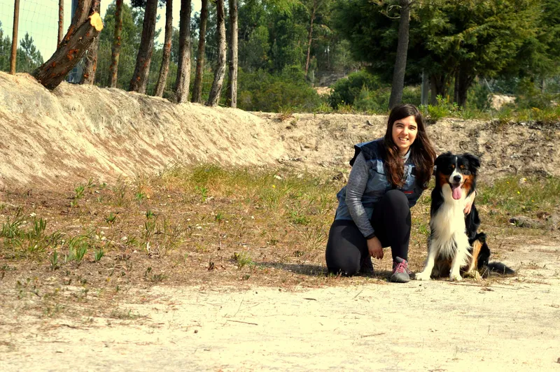 Ana Martins agachada com um Border Collie e um Jack Russell no campo de treino da Dream Dogs